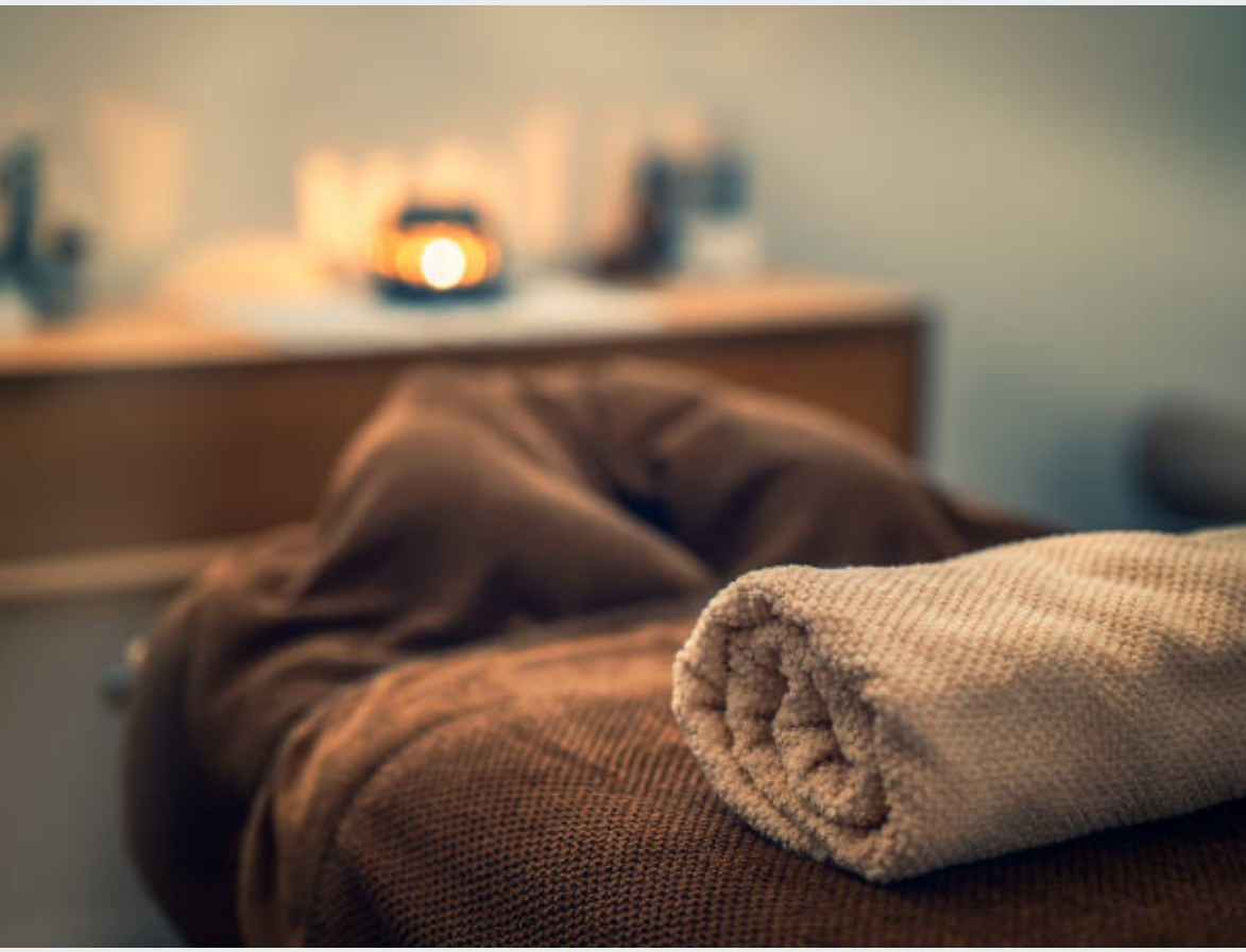 A calm treatment room with a massage table and a folded towel in focus.